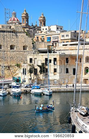 SENGLEA, MALTA - MARCH 31, 2017 - Passengers on board a traditional Maltese Dghajsa water taxi in the harbour with views towards Senglea waterfront Vittoriosa Malta Europe, March 31, 2017.