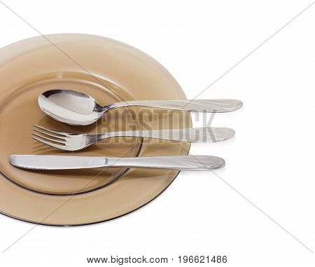 Fragment of the dark glass dish and eating utensils consisting of spoon fork and knife made from stainless steel on it closeup on a light background