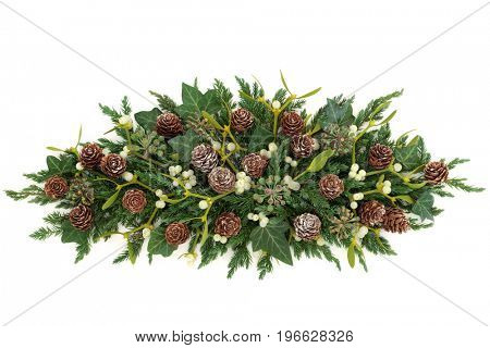 Winter greenery display with mistletoe, juniper fir, ivy and pine cones forming a centrepiece on white background.