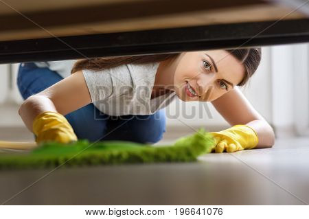 young woman in protective gloves cleaning floor under bed with mop. Housework, housekeeping and wet cleaning concept