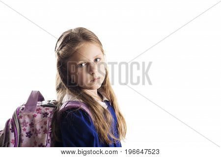 A sad caucasian elementary age schoolgirl with glasses posing in uniform and backpack isolated on white background. School and education concept.