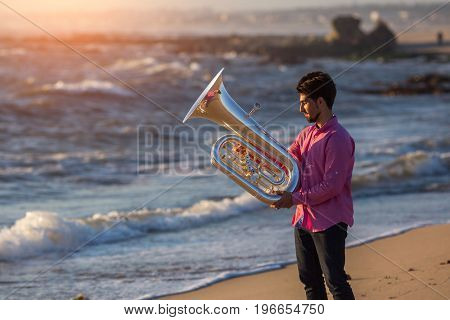 Young man with trumpet on the sea coast during surf. Tuba instrument. 