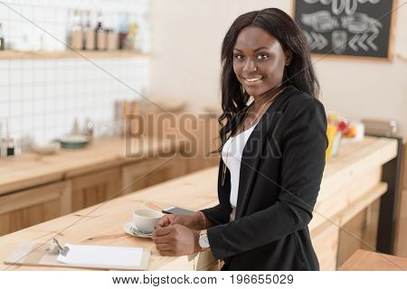 Attractive African American Woman With Coffee Cup And Bill Looking At Camera In Cafe