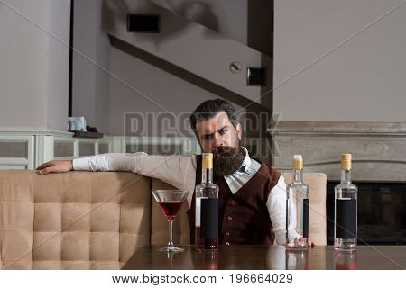 Man drinking red wine alone in restaurant. Bearded hipster with beard sitting at table with three bottles and glass. Alcohol abuse. Addictive and convive. Unhealthy lifestyle and bad habits