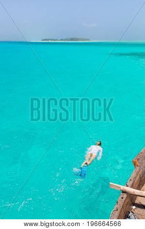 Woman snorkeling in clear shallow sea of tropical lagoon with turquoise blue water and coral reef, near exotic island. Mnemba island, Zanzibar, Tanzania.