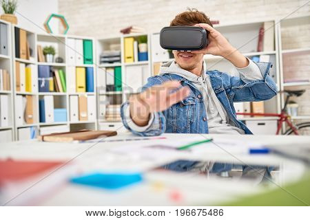 Portrait of young man dressed in casual jeans clothes using virtual reality glasses  in office , taking a break to enjoy 3D game experience