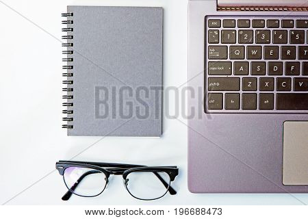Top view of business working place with notepadmodern glasseskeyboard on white tableflatlay concept.