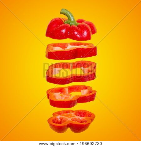 Flying red capsicum. Sliced floating bell pepper on an orange background. Levity vegetable. Paprika with water drops