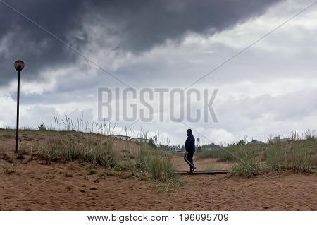 A man walking away from the beach of Kalajoki Finland. The weather was cold and rainy and quickly getting worse. The man is hurrying to a warmer place.