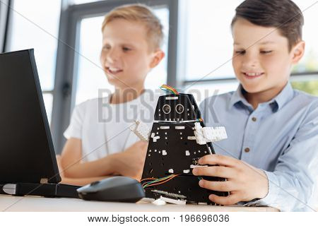 Pleasant time together. Two lovely pre-teen boys sitting at the table and watching a film on the laptop while one of the boys playing with a black robot model