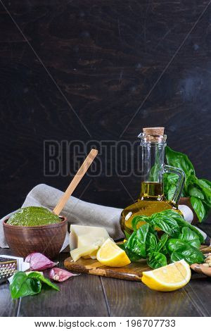 Tradizione Italiana Homemade Pesto recipe ingredients on dark table. Parmesan cheese, basil leaves, pine nuts, olive oil, garlic.