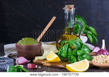 Tradizione Italiana Homemade Pesto recipe ingredients on dark table. Parmesan cheese, basil leaves, pine nuts, olive oil, garlic.