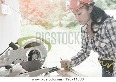 Pretty Asian carpenter woman is marking on wood for cut.