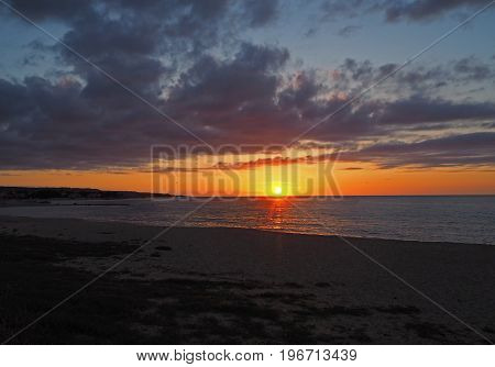 Sunset With The Red Orange Sun Going Down To The Sea On The Sand Beach With Dark Cloudes