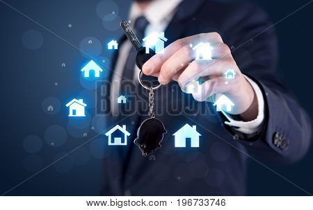 Businessman in suit holding keys with house graphics around and dark background