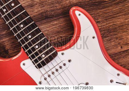 Part of modern electric six string guitar red color with glossy finish pickups and control knobs isolated on wooden background close up view.