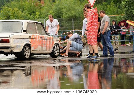 Orel Russia July 22 2017: Dynamica car festival. Young people looking at old Soviet car VAZ Lada with graffiti near big water puddle at rainy day