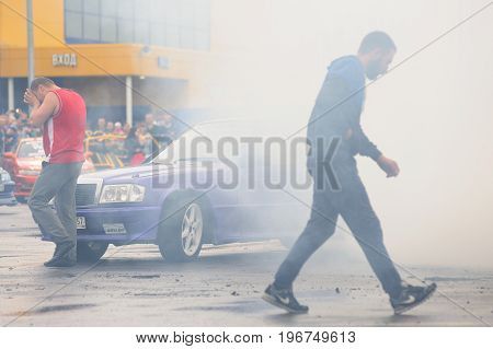 Orel Russia July 22 2017: Dynamica car festival. Man walking in burning wheel smoke clouds background
