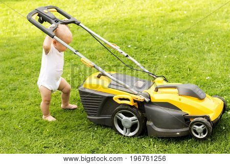 Funny baby boy cuts the lawn with a grassmower.