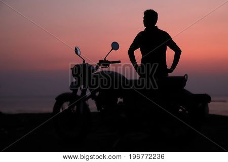 Young man standing near motorbike and enjoying sunset view