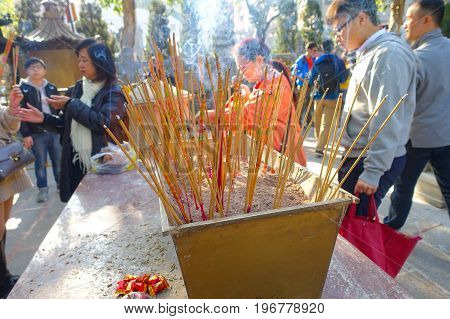 HONG KONG, CHINA - JANUARY 22, 2017: Close up of incenses burning up, with people behind of Wong Tai Sin Buddhist Temple to pray, in Hong Kong, China.