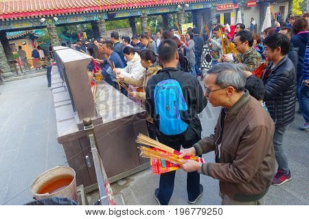 HONG KONG, CHINA - JANUARY 22, 2017: Crowd of people holding a their hands an incense sticks in a sunny day, inside of Wong Tai Sin Buddhist Temple to pray, in Hong Kong, China.