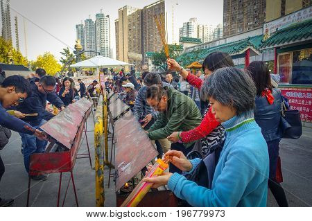 HONG KONG, CHINA - JANUARY 22, 2017: Crowd of people holding a their hands an incense sticks in a sunny day, inside of Wong Tai Sin Buddhist Temple to pray, in Hong Kong, China.