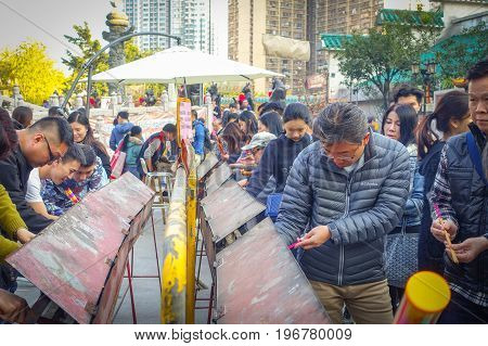 HONG KONG, CHINA - JANUARY 22, 2017: Crowd of people holding a their hands an incense sticks in a sunny day, inside of Wong Tai Sin Buddhist Temple to pray, in Hong Kong, China.