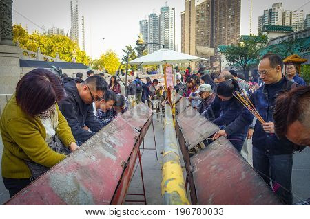 HONG KONG, CHINA - JANUARY 22, 2017: Crowd of people holding a their hands an incense sticks in a sunny day, inside of Wong Tai Sin Buddhist Temple to pray, in Hong Kong, China.