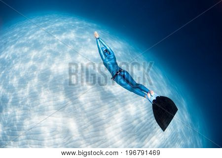 Woman freediver glides over sandy sea bottom with monofin