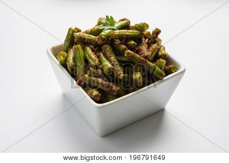 A Masala or fried vegetable dish consisting of green beans, onions, and curry spices, served in square bowl, selective focus