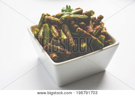 A Masala or fried vegetable dish consisting of green beans, onions, and curry spices, served in square bowl, selective focus