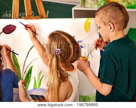 Children painting on easel. Girl with boy learn paint in class school. Child picture on background. Preparing for a children's art exhibition.