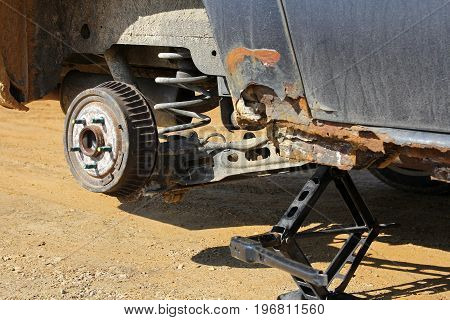 A rusty old car is raised up on a jack for a tire change after getting a flat tire.