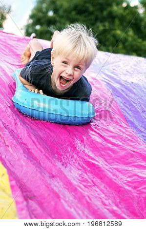 A happy young child is screaming as he slides down a slip-and-slide in his backyard.