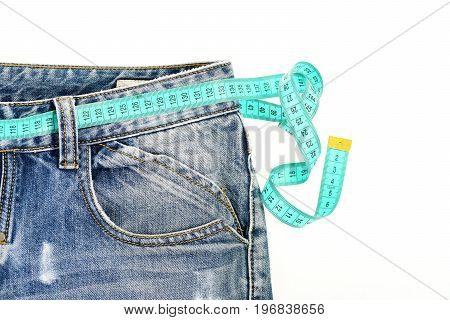 Blue jeans with blue measure tape instead of belt. Healthy lifestyle and dieting concept. Close up of jeans with measure tape around waist. Upper part of denim trousers isolated on white background.