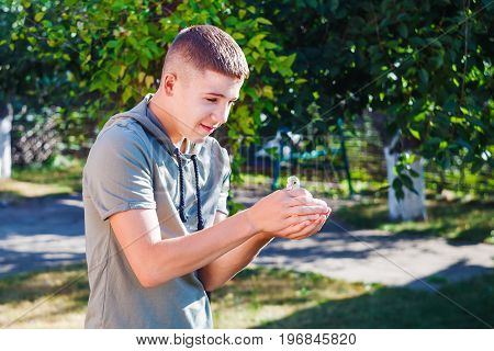 The boy carefully keeps the duckling in his hands and smiles happily.