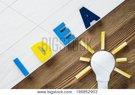Lightbulb and idea word on the wooden background. Colorful word IDEA on two color wooden background. The concept of creativity.