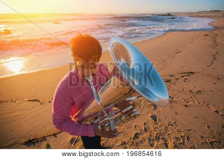Young musician playing the trumpet on the sea coast. 