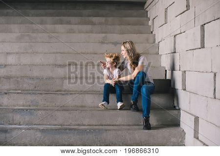 Mother with son sitting on a stairs and looking somewhere