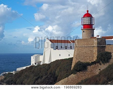 red lighthouse on Cabo de Sao Vicente with stone wall and white house