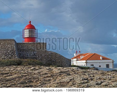 red lighthouse on Cabo de Sao Vicente with stone wall and house and blue sky