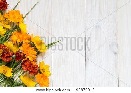Calendulae and marigolds on a light wooden background.