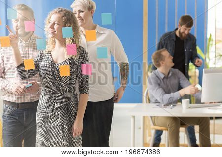 Team of coworkers going through colorful sticky notes on a glassboard
