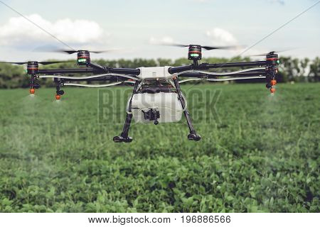 Agriculture drone spraying water or pesticides to grow over green field. Smart farming concept.