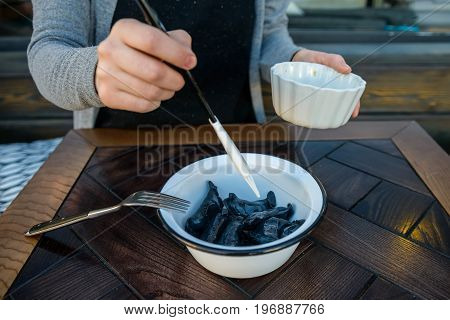 Close up female hands adding butter with a brush to bowl full of black dumplings traditional Russian dish
