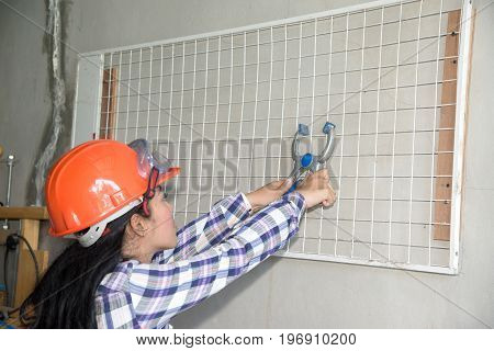 Young beautiful Asian woman holding and install white plastic mesh with pliers on the wall in shop.