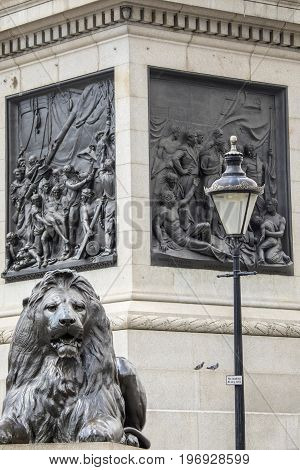 One of the iconic Lions at the base of Nelsons Column in Trafalgar Square in London UK. The sculptured scenes behind the Lion portray moments from the Naval career of Lord Horatio Nelson.