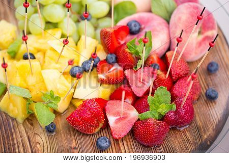 Festive food. Canape with fruits. bunch of grapes, juicy peaches, fresh mint, sweet pineapple, bright strawberry. The taste of summer and fresh fruit