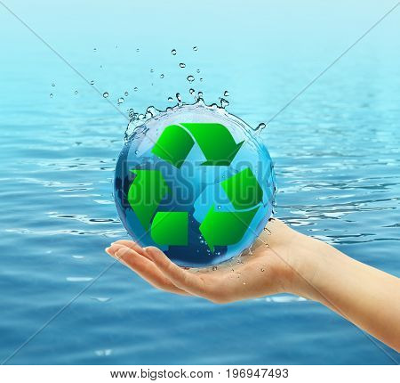 Female hand holding globe and sign of recycling on water background. Ecology and environment conservation